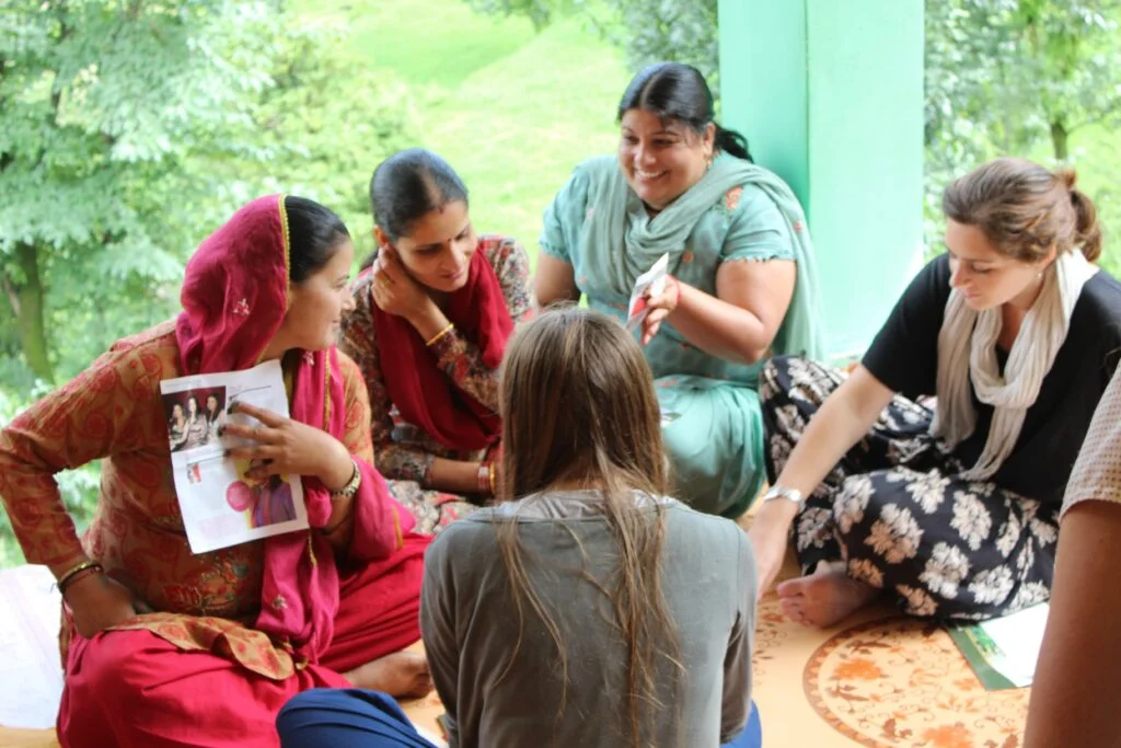 A CIEEL fellow seated on a verandah with rural women from a Self-Help Group at Naddi, Kangra, in animated conversation around printed materials
